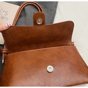 Detail view of brown textured leather baguette bag with magnetic snap closure and slim strap
