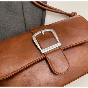 Detail of vintage brown leather baguette bag with shiny silver square buckle and stitching