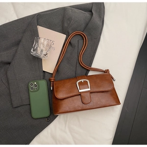 Flat lay of retro brown matte leather shoulder bag with silver horseshoe buckle and grey suit