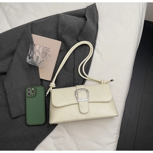 Detail of creamy white leather baguette bag with silver buckle on a minimalist bedding