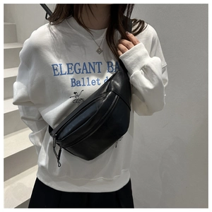 Detail of a black PU leather crossbody bag with dual zippers worn by a model on stairs