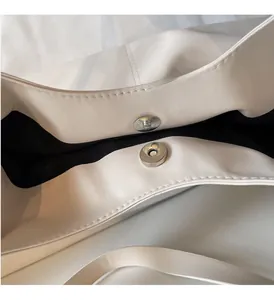 Close-up of dual silver magnetic buckles and fine stitching on white shoulder bag