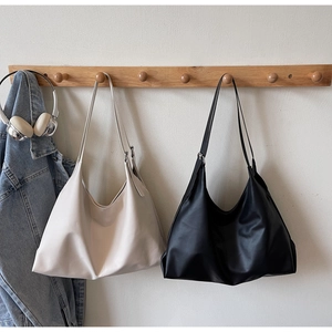 Close-up of minimalist hobo tote bags in cream and black hanging on wooden hooks