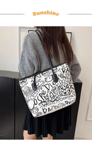 Detail view of large white tote bag with black graffiti prints worn by a model