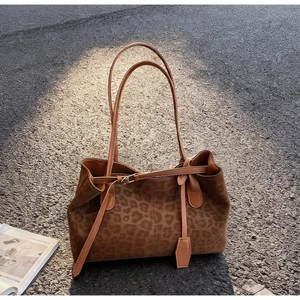 Close-up of leopard print tote bag with brown leather handles on asphalt surface