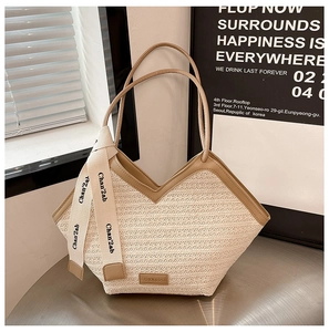 Detail of woven straw tote bag with brown PU leather trim and branded decorative ribbon