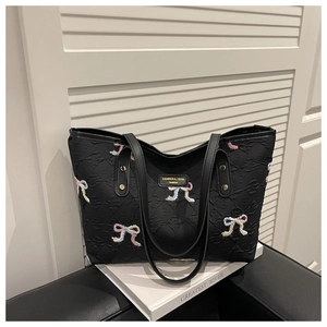 Detail of embroidered colorful bows and quilted diamond texture on a black tote bag