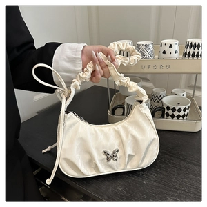 Detail of a creamy white pleated handbag with a metallic silver butterfly ornament