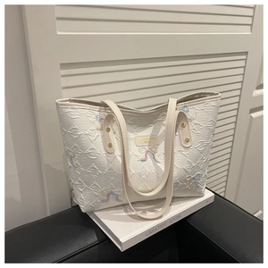 Detail of white quilted tote bag featuring colorful embroidered bows and metal logo charm