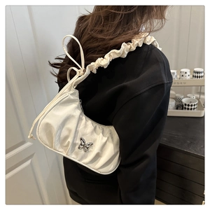 Detail of white pleated handbag featuring a silver butterfly buckle and ruffled strap