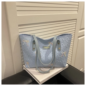 Detail of light blue tote bag with embossed texture and embroidered bow accents
