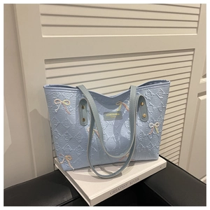Detail of light blue quilted tote bag with embroidered bows and metal logo plaque