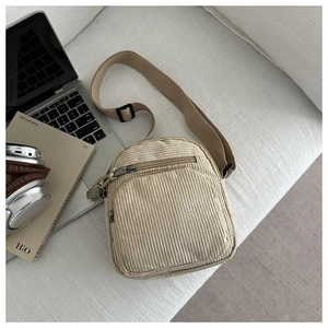 Détail d'un petit sac bandoulière en velours côtelé beige avec poche zippée sur canapé