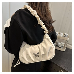 Detail of white pleated crescent shoulder bag with silver butterfly and ruffled strap