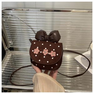Détail d'un sac marron à pois pour enfants avec nœud en cuir et fleurs en peluche rose
