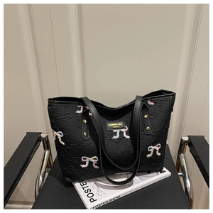 Close-up of black quilted tote bag featuring a colorful sequined bow and leather logo