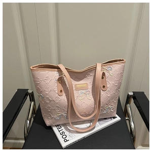 Close-up of pink quilted tote bag with colorful embroidered bows on a leather chair