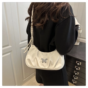Detail of cream pleated underarm bag featuring a metallic butterfly clasp and satin finish