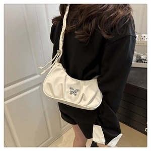 Detail of cream pleated shoulder bag featuring a silver butterfly buckle and thin strap