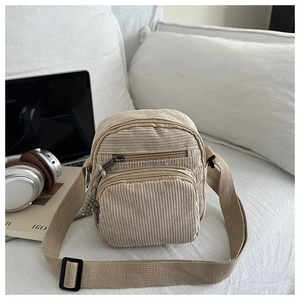 Gros plan du sac de téléphone en velours côtelé beige avec trois poches zippées sur canapé
