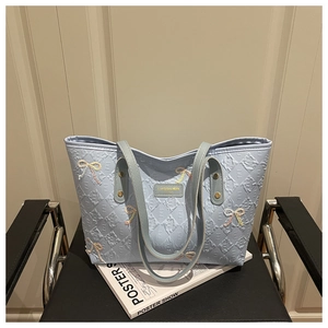 Macro detail of quilted light blue tote bag featuring beaded bow and gold logo plate