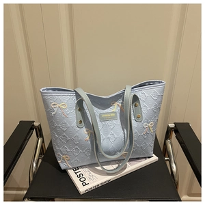 Close-up of light blue quilted tote bag featuring embroidered bows and gold logo