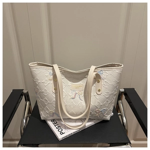 Close-up of quilted tote bag featuring embroidered bows and premium metal logo plate