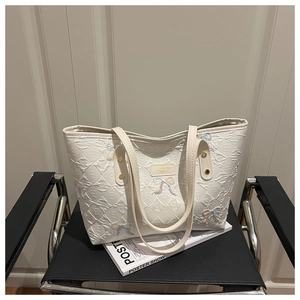 Close-up of quilted white tote bag featuring embroidered bow detailing and gold rivets