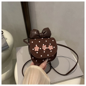 Détail d'un sac bandoulière enfant marron à pois avec un grand nœud et des fleurs en peluche