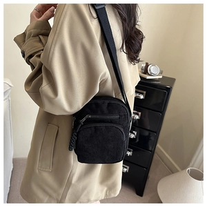Sac bandoulière en velours côtelé noir porté avec un trench-coat beige élégant