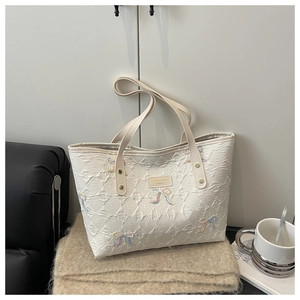 Detail of embroidered bow patterns on cream quilted tote bag with diamond stitching