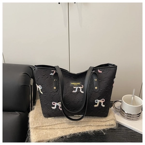 Detail of embroidered bows on black quilted tote bag with soft lifestyle background