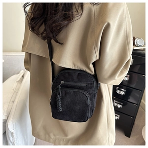 Détail d'un sac bandoulière en velours côtelé noir porté avec des tirettes tressées