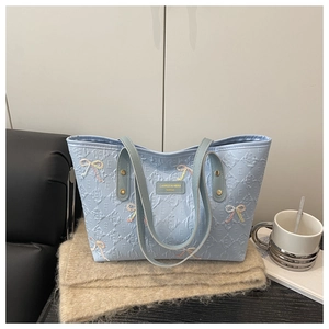 Close-up of embroidered bow details and textured diamond pattern on the light blue tote bag