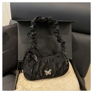 Detail of black pleated shoulder bag featuring a prominent silver metal butterfly ornament