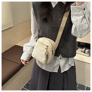 Détail d'un sac bandoulière en velours côtelé beige avec large sangle porté par un mannequin