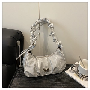 Close-up of silver pleated underarm bag with metallic butterfly charm and ruched strap