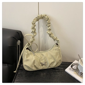Close-up of a light green pleated hobo bag featuring a silver metal butterfly ornament