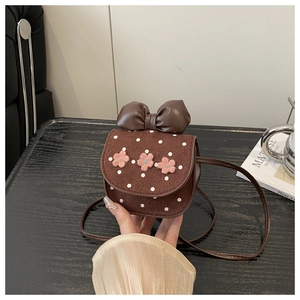 Détail d'un mini sac bandoulière marron à pois avec un nœud et des fleurs roses