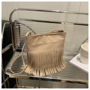 Detail of bohemian apricot shoulder bag with long fringe tassels on minimalist shelf