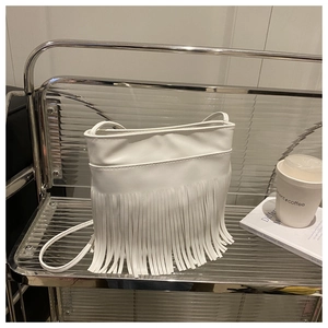 Close-up of white tassel crossbody bag on a modern stand with coffee and lifestyle props