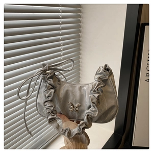 Detailed view of silver pleated handbag featuring a metallic butterfly ornament