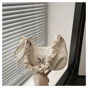 Macro detail of creamy satin crescent bag featuring pleated strap and silver butterfly buckle