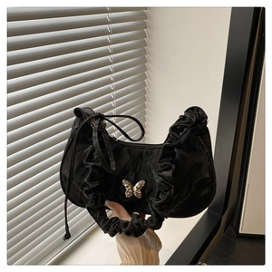 Detail of black pleated shoulder bag featuring a silver metal butterfly ornament