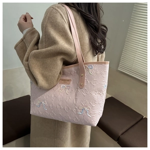 Close-up of pink quilted tote bag featuring embroidered bows and slim shoulder strap