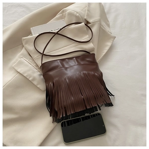 Detailed close-up of brown fringe crossbody bag with PU leather tassels on beige blazer