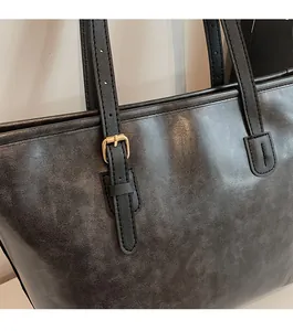 Close-up of vintage leather texture and gold buckle hardware on a dark grey tote bag