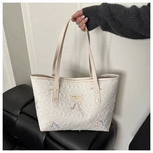 Detail of white quilted tote bag featuring colorful bow embroidery and gold-tone nameplate