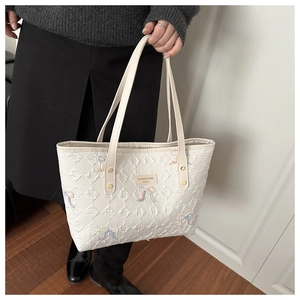 Detail of white quilted tote bag featuring colorful bow embroidery and brand name plate