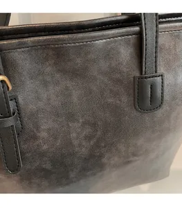 Detail of grey tote bag showing matte faux leather texture and gold lettering print